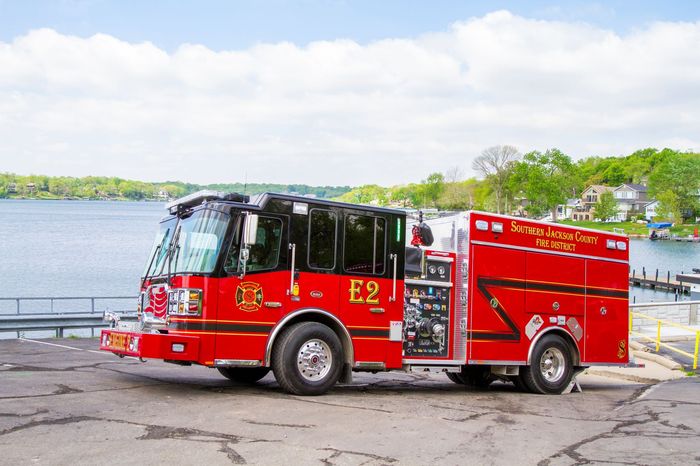 Red fire truck parked beside a lake on a sunny day