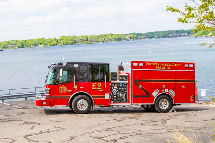 Red fire truck parked by a lakeside with water and trees in the background
