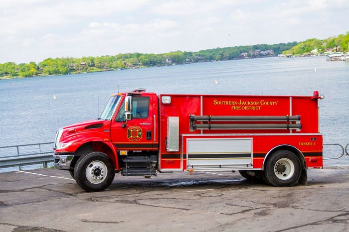 Red fire truck parked on a waterfront road beside a calm lake.