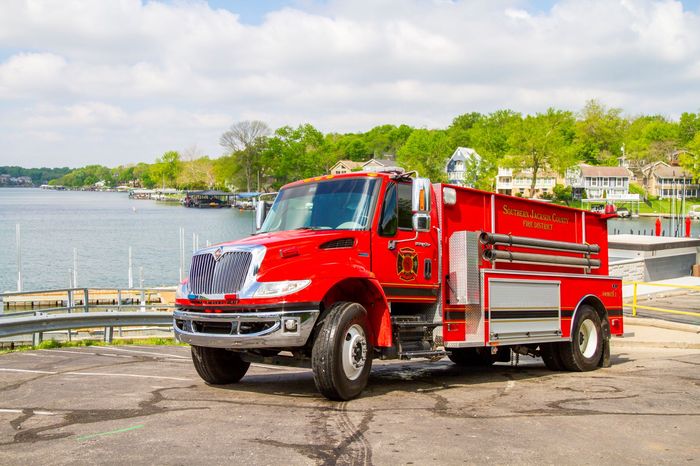 Red fire truck parked by a lakeside road under a bright sky
