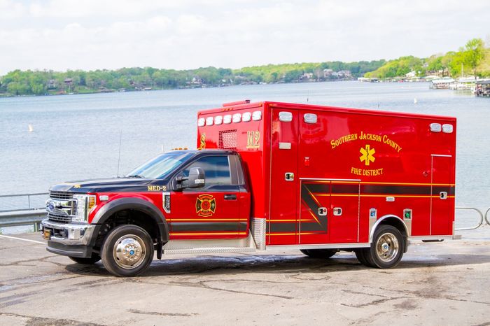 Red ambulance parked by the water on a shoreline road