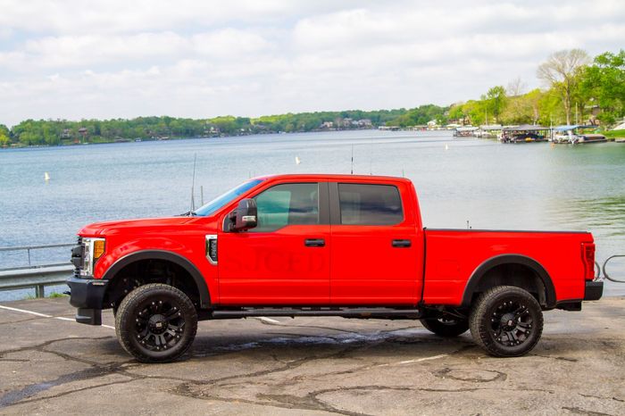 Red pickup truck parked by a lakeside road under a cloudy sky