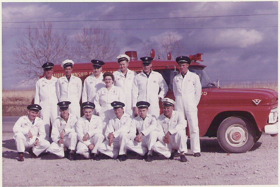 Group of uniformed people posing in front of a red truck in a parking lot.