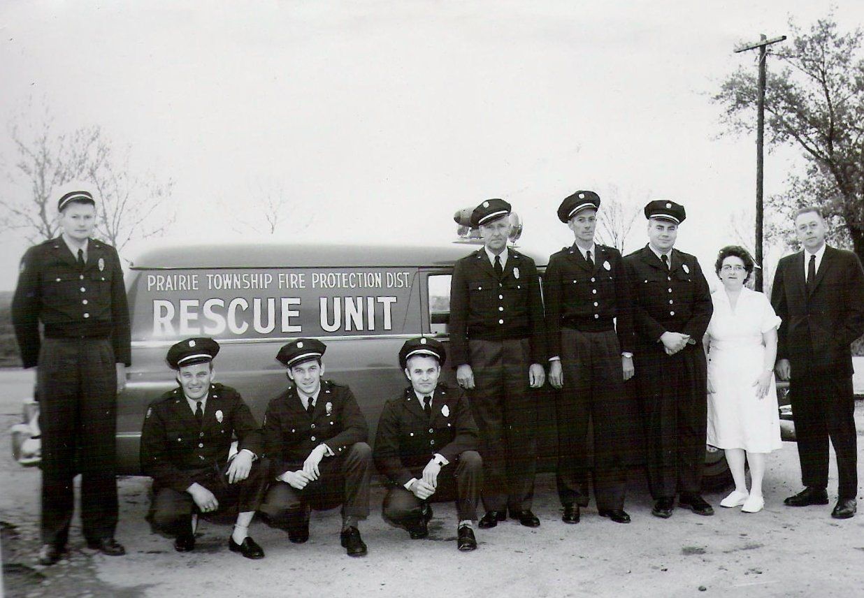 Group of rescue unit members posing outdoors beside a “RESCUE UNIT” sign and a small aircraft
