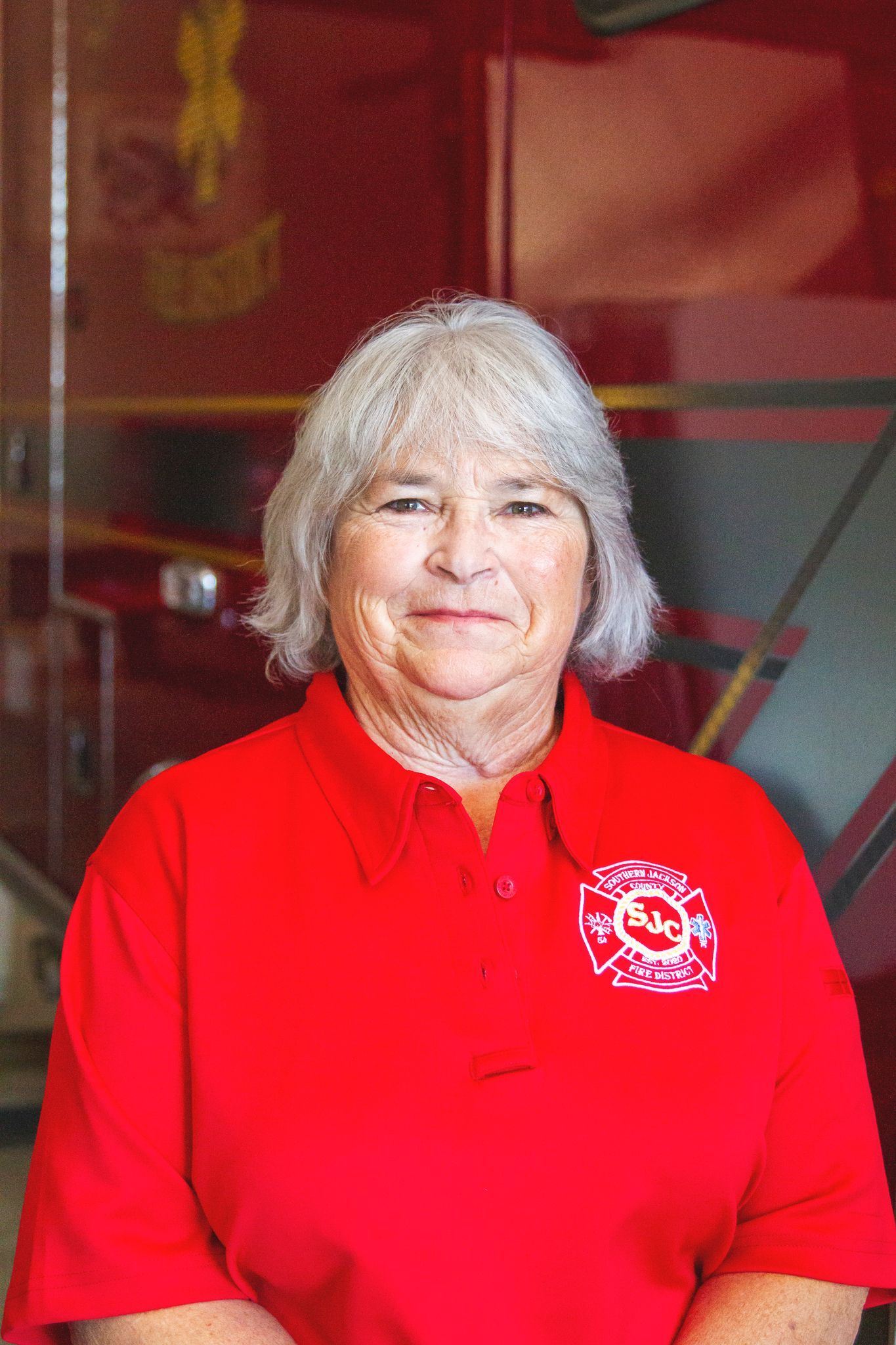 Smiling person in a red polo shirt standing indoors against a red and gray background