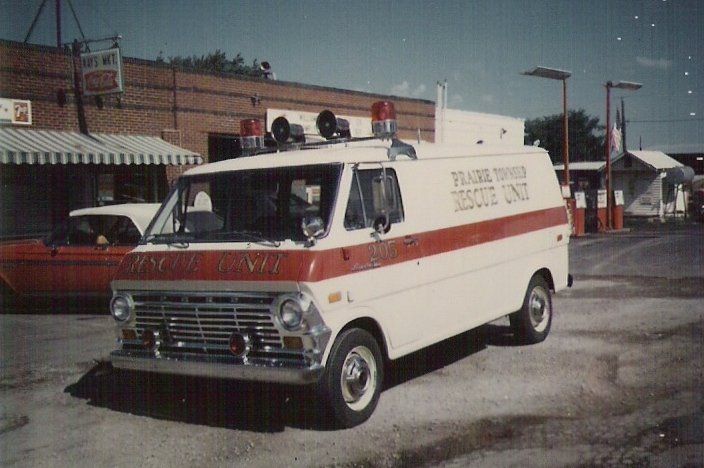 White fire rescue van with red stripe parked outside a building, emergency lights on top