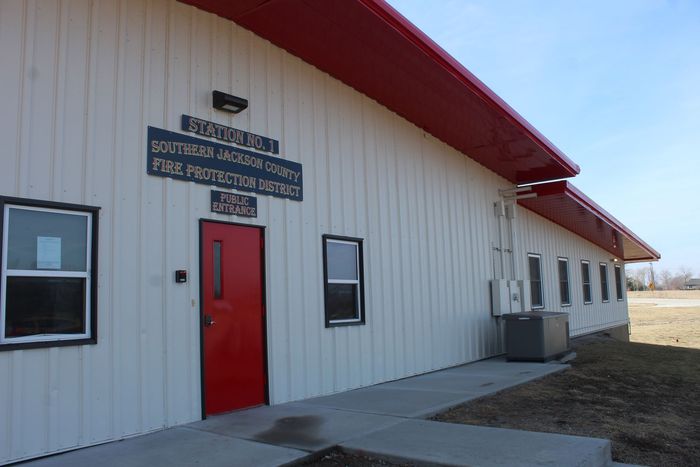 White building with red roof and door, sign above entrance, and sidewalk along the side