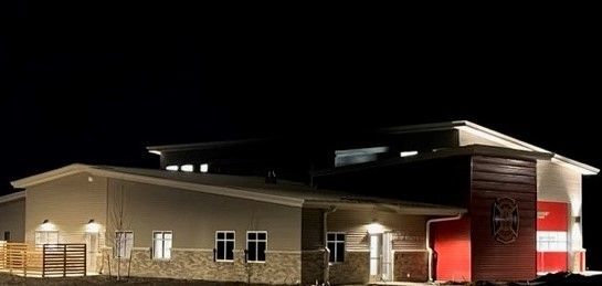Nighttime exterior of a brick building with lit windows and a bright red entrance