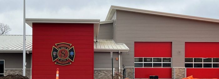 Red fire station building with large garage doors and a fire department emblem on the front.