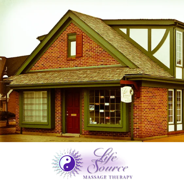 A brick building with green trim and windows, featuring a sign for Life Source Massage Therapy.