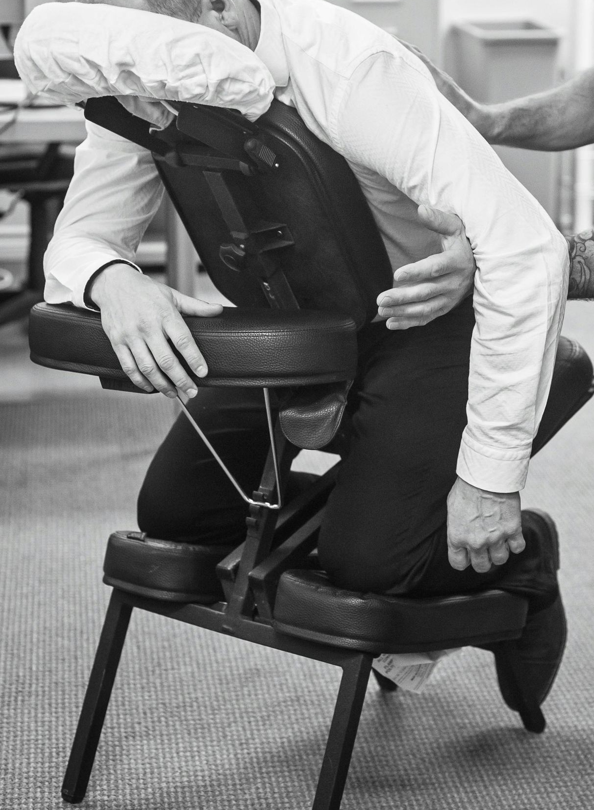 A person in business attire receives a professional massage while resting on a portable ergonomic massage chair.