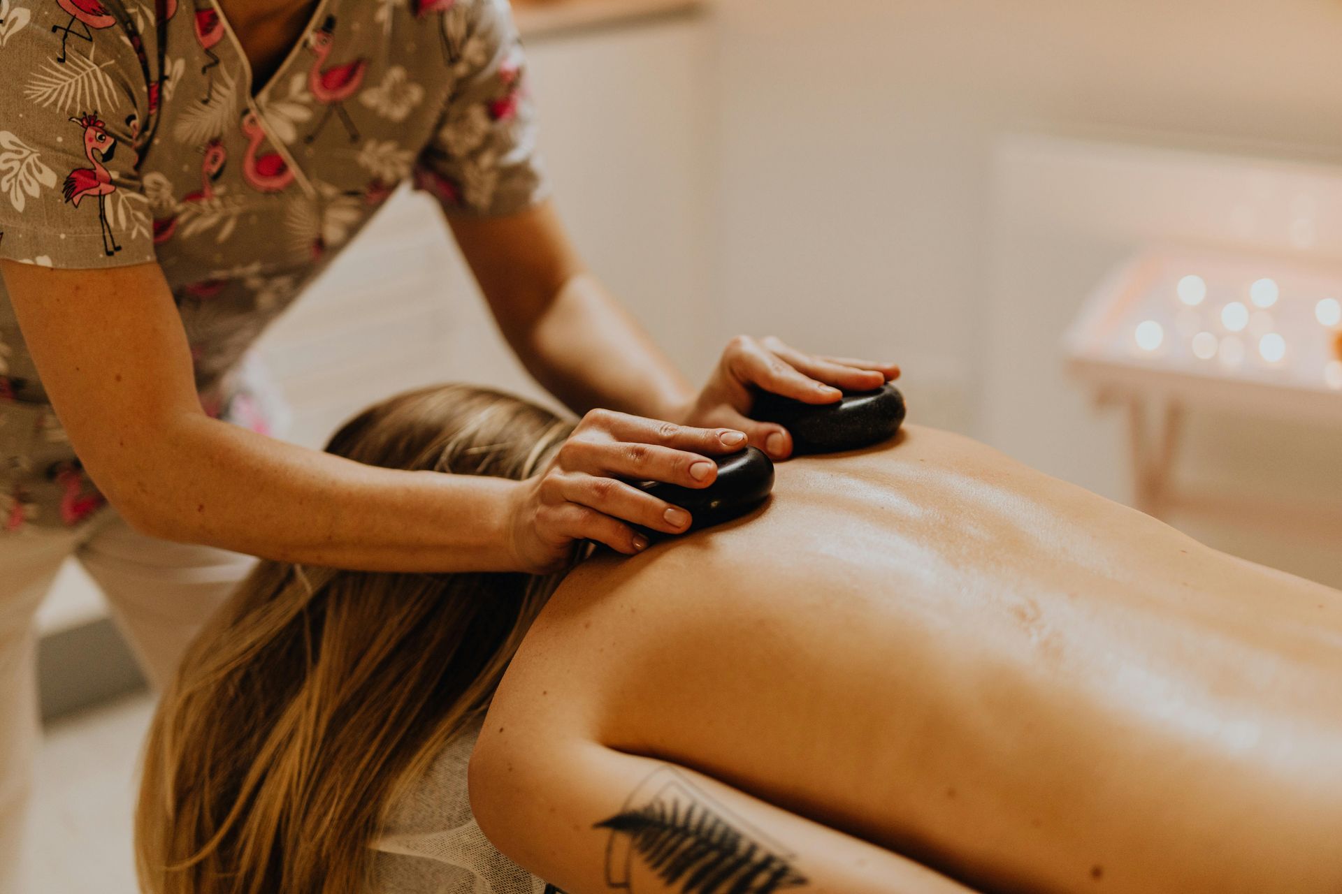 A person receives a warm stone massage on their back in a tranquil spa setting.