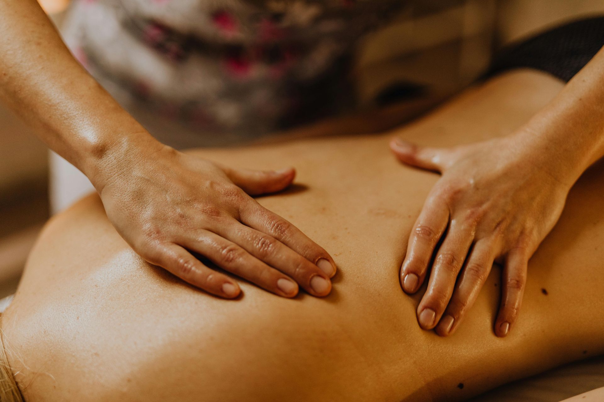 A person's hands perform a massage on a person's bare back, with oil glistening on the skin.