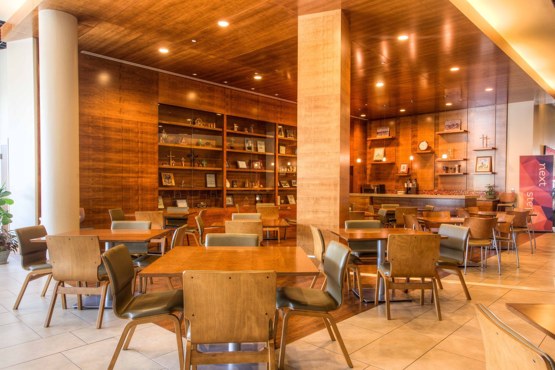 Wooden-paneled cafe interior with tables and chairs, a bookcase, and overhead lighting.