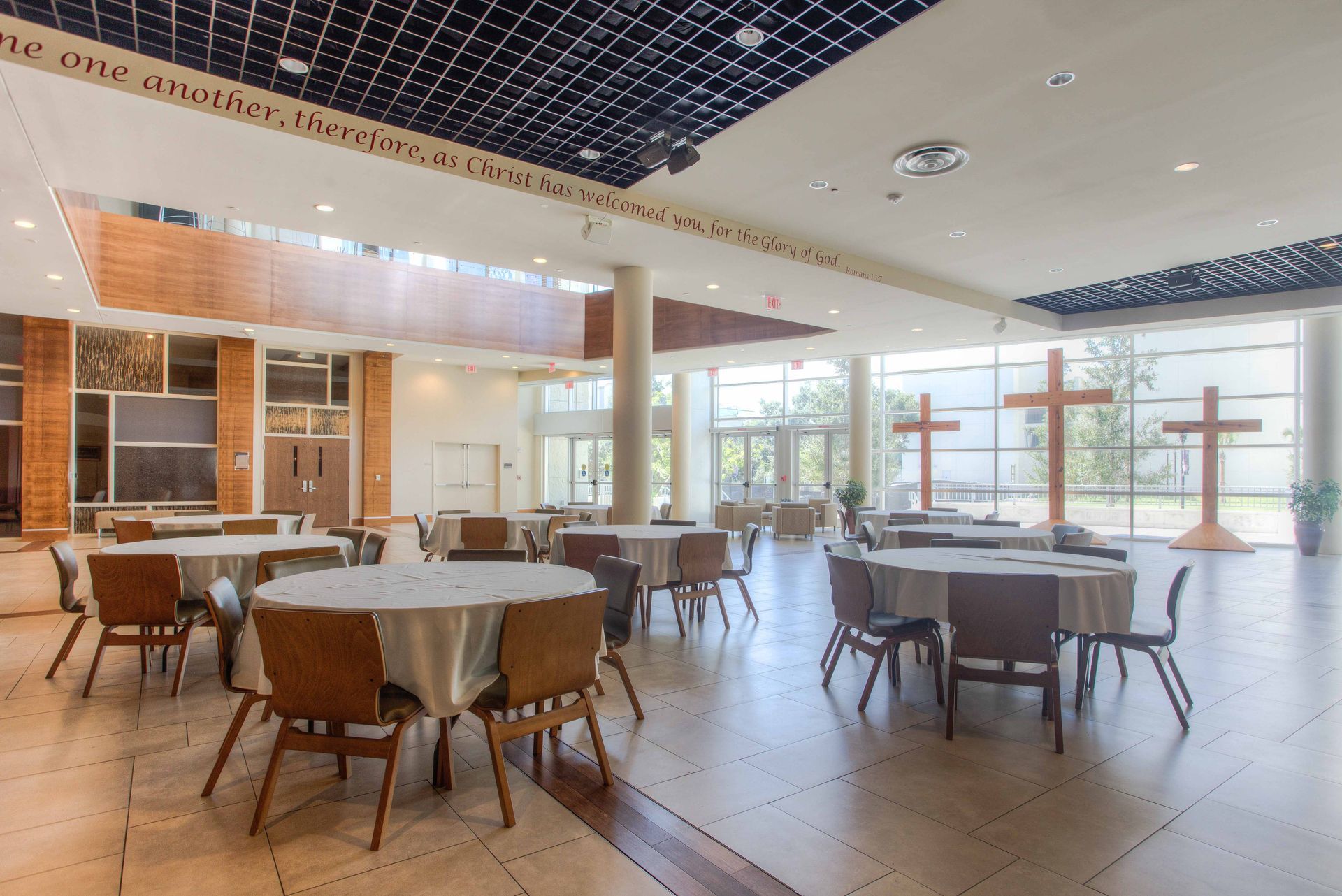A large, bright room with round tables, chairs, and large wooden crosses; likely a church or event space.