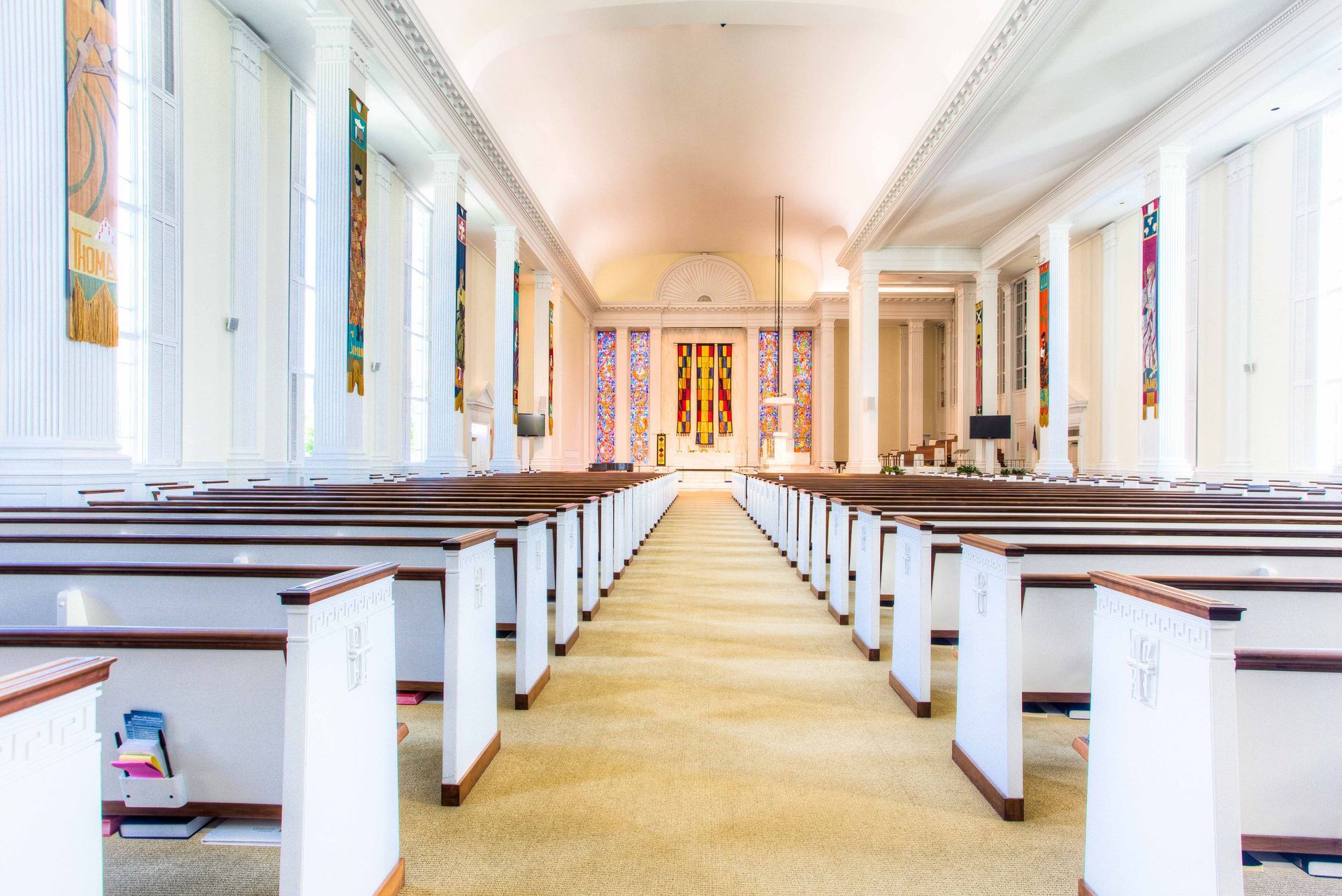 Interior of a synagogue with rows of pews facing the Torah ark; stained glass windows.