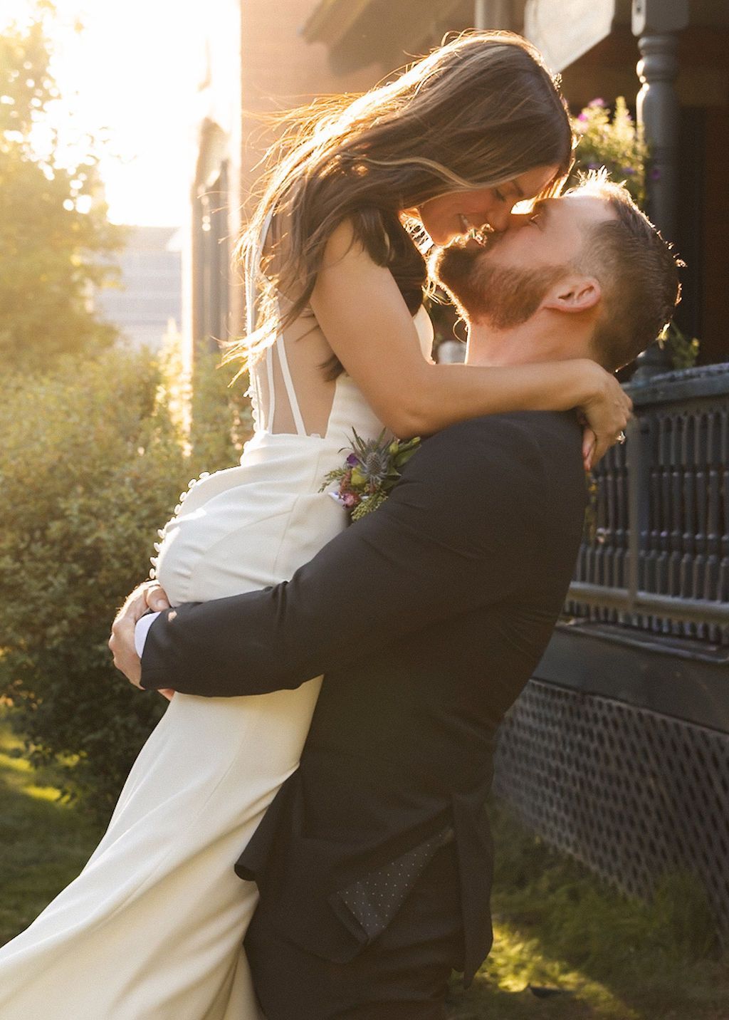 Couple embracing and kissing outdoors at sunset, the woman in a white dress and the man in a black suit