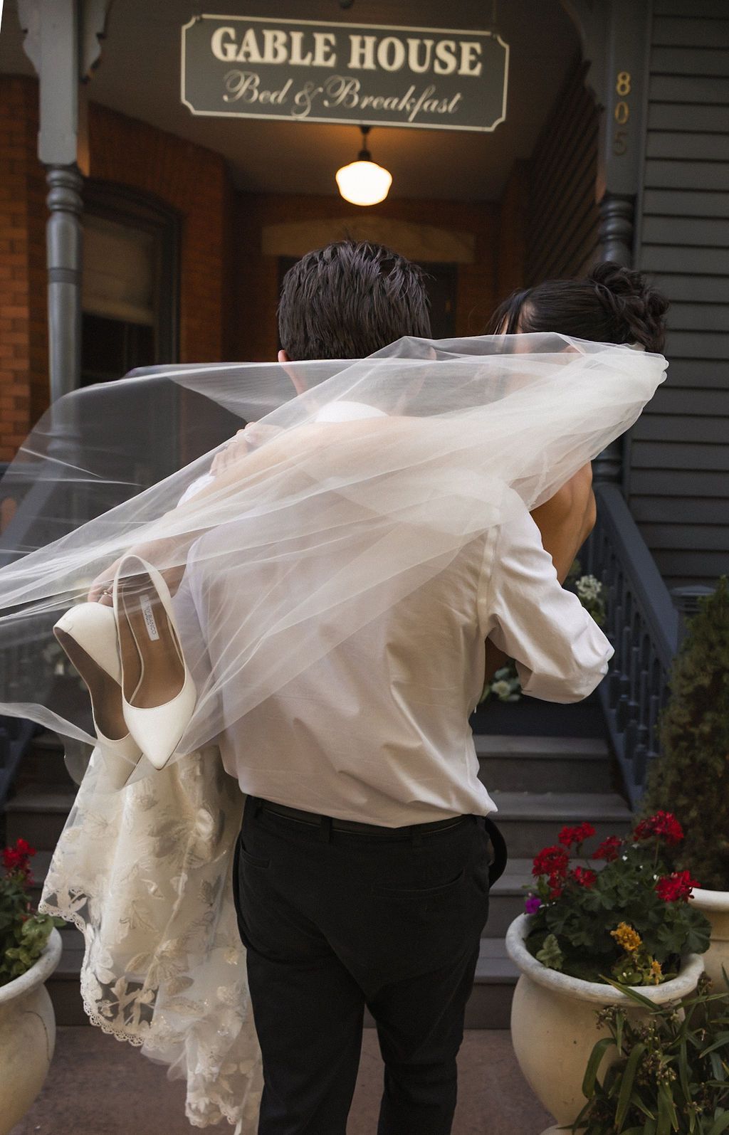 Bride and groom walking into Gable House, bride's veil blowing across them.