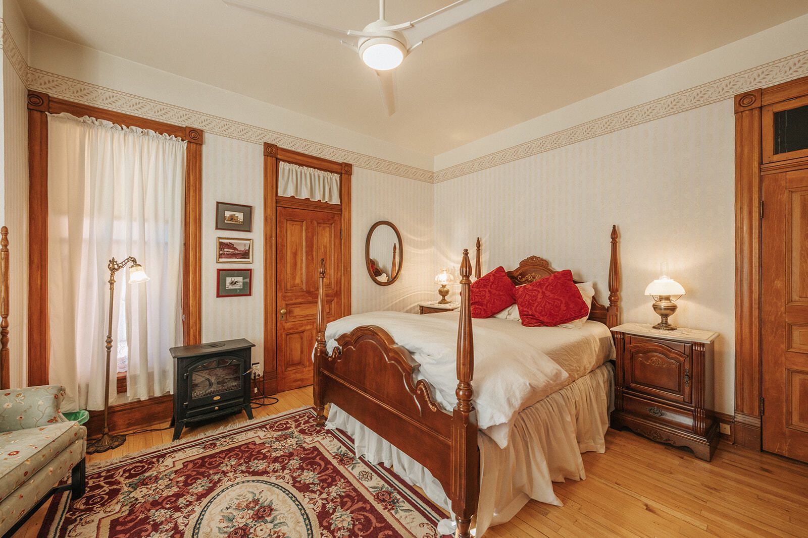 Cozy bedroom with a wooden bed, red bedding, ornate rug, and curtains by tall windows