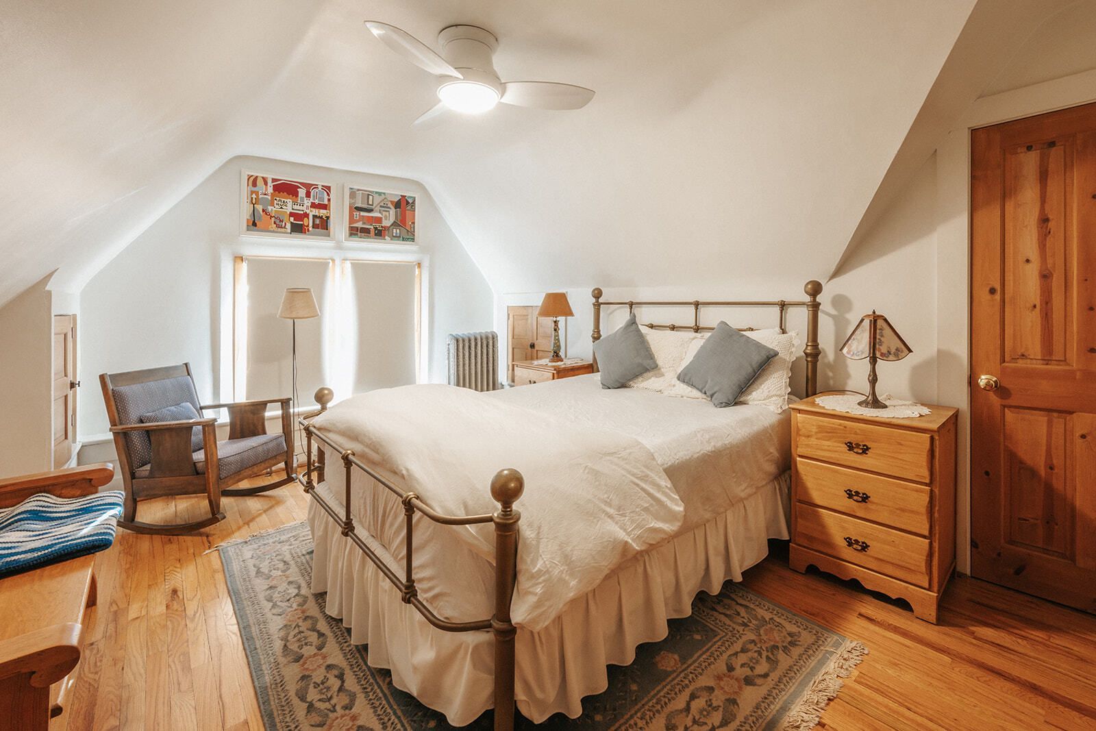 Cozy attic bedroom with a brass bed, wooden furniture, skylight, and sloped white ceiling