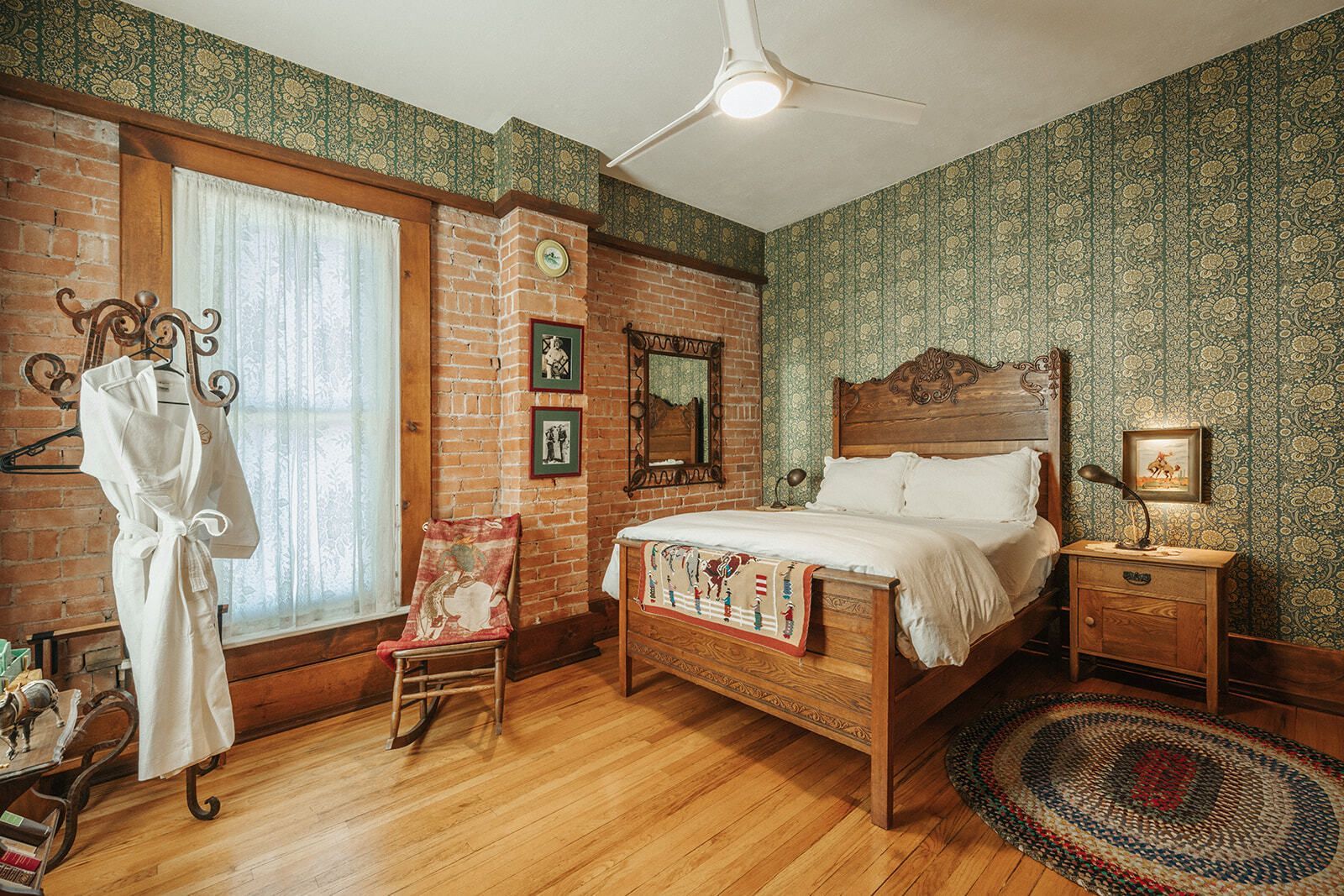 Vintage bedroom with wooden bed, patterned green wallpaper, bay window, rocking chair, and rug