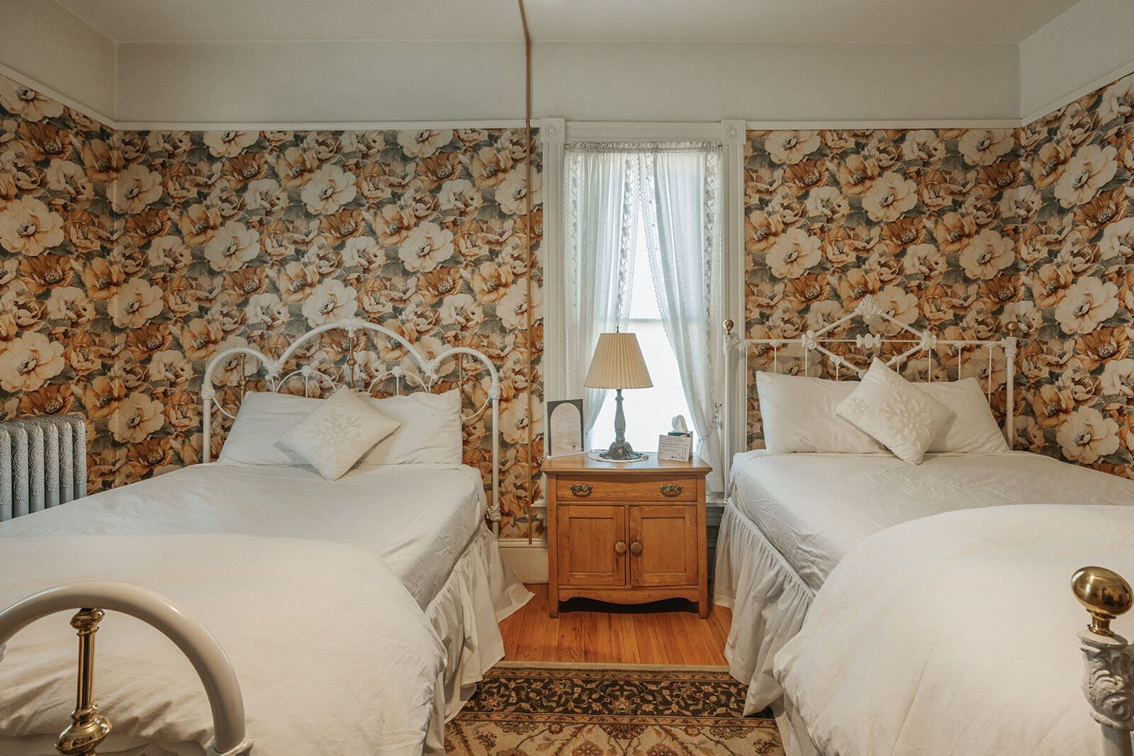 Cozy bedroom with two twin beds, floral wallpaper, and a nightstand between a window