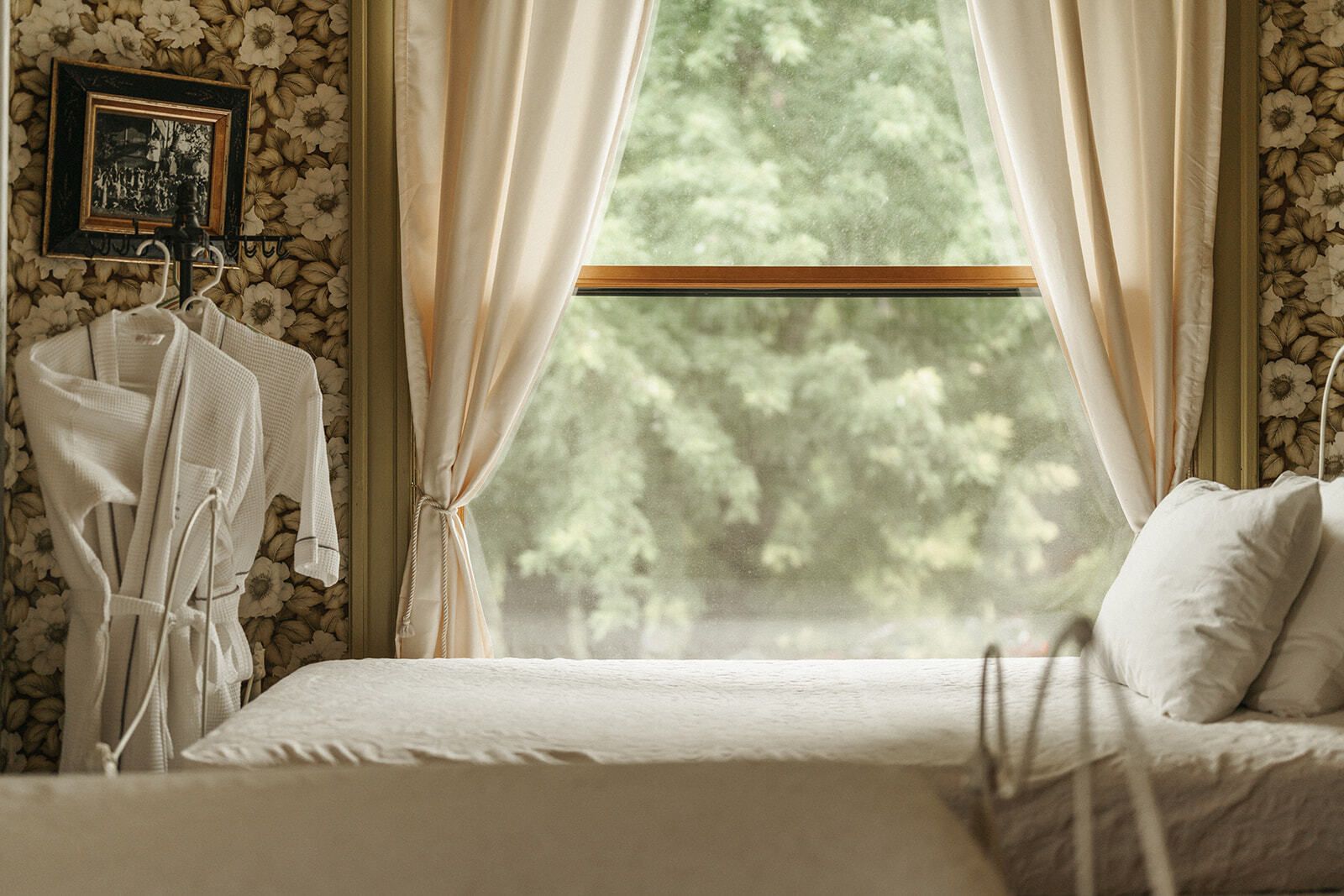 Cozy bedroom with a bed, mannequin, and large window with cream curtains and greenery outside