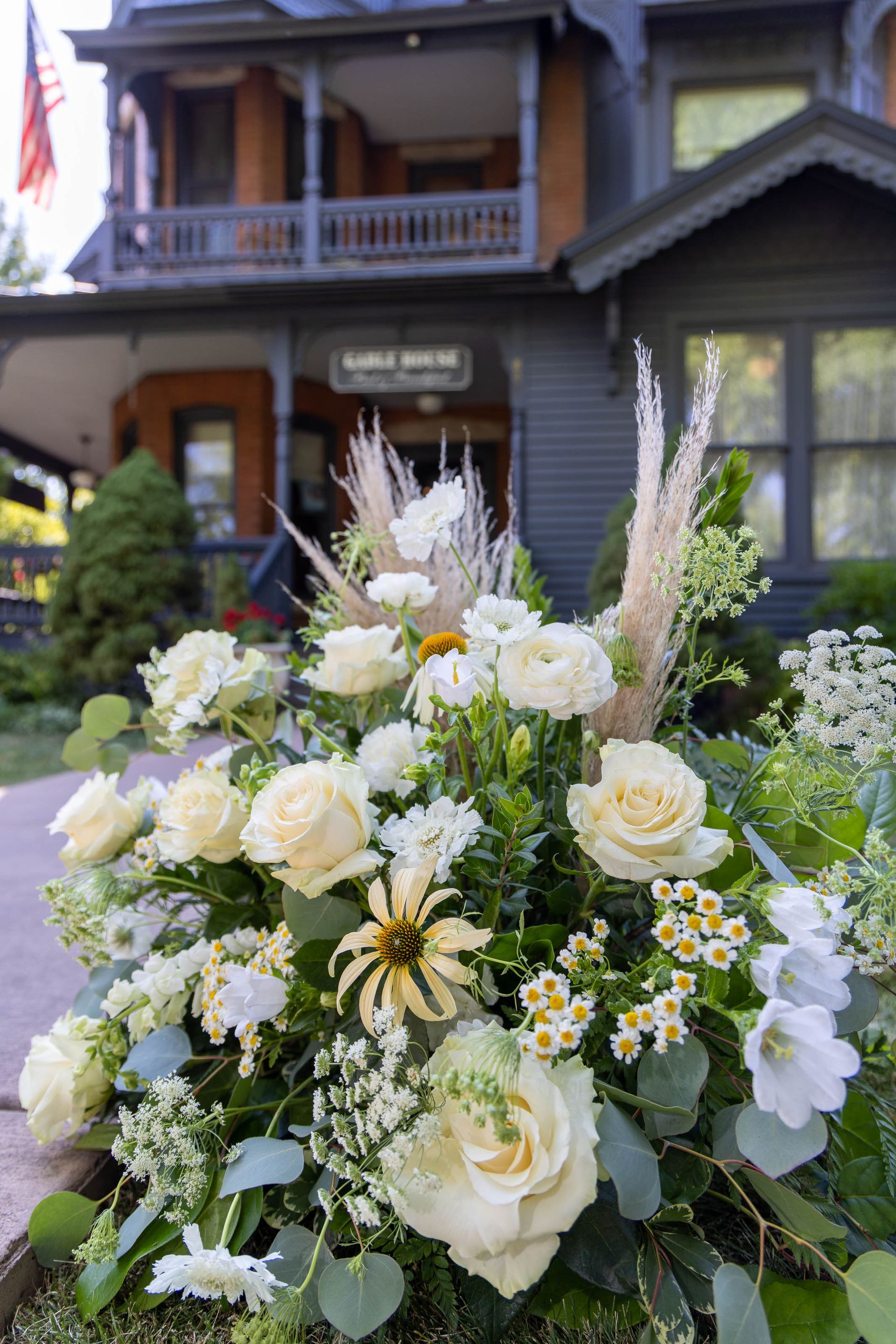 White and pale yellow floral arrangement in front of a dark house with a porch