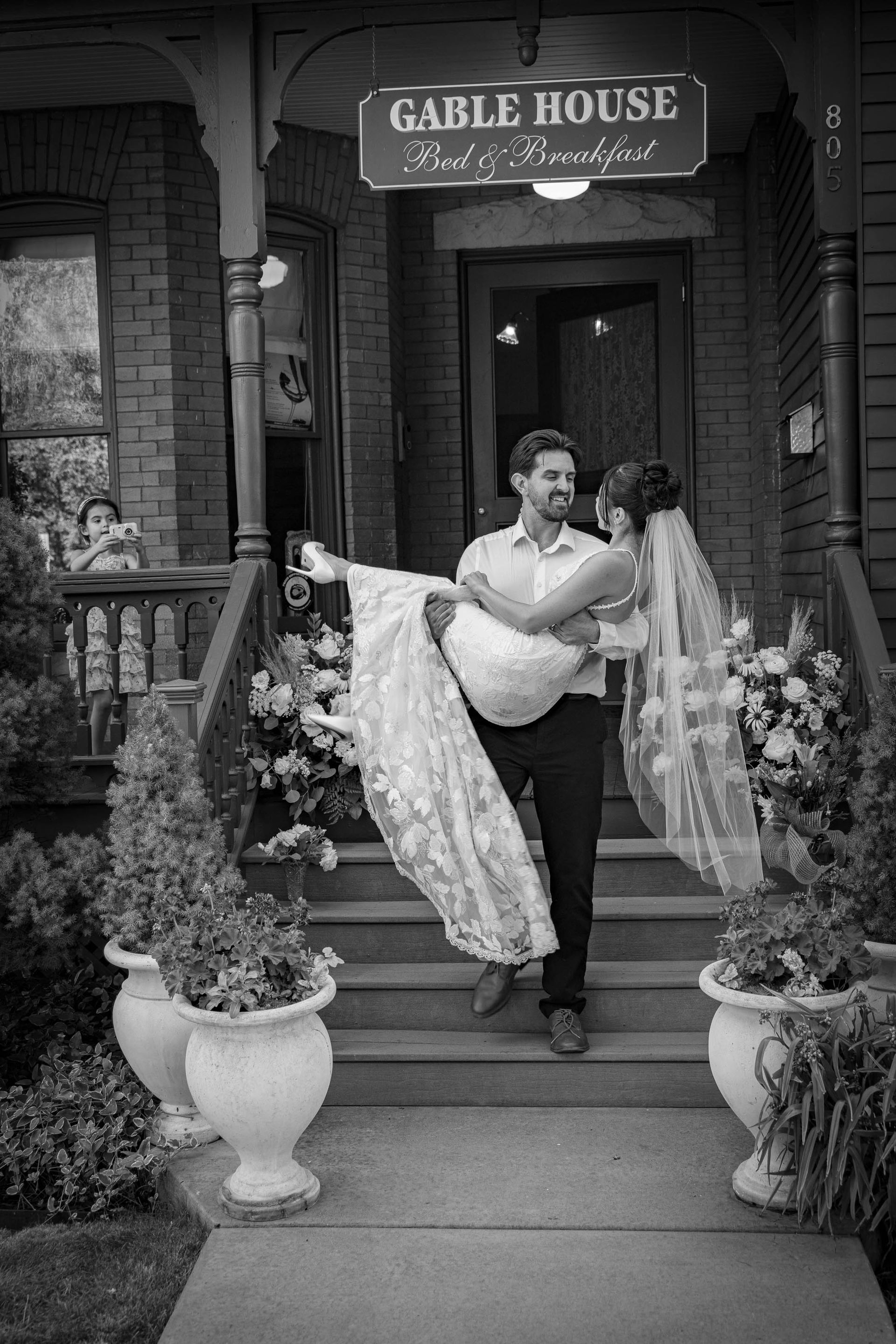 Bride being carried in front of Gable House’s entrance, framed by floral arrangements