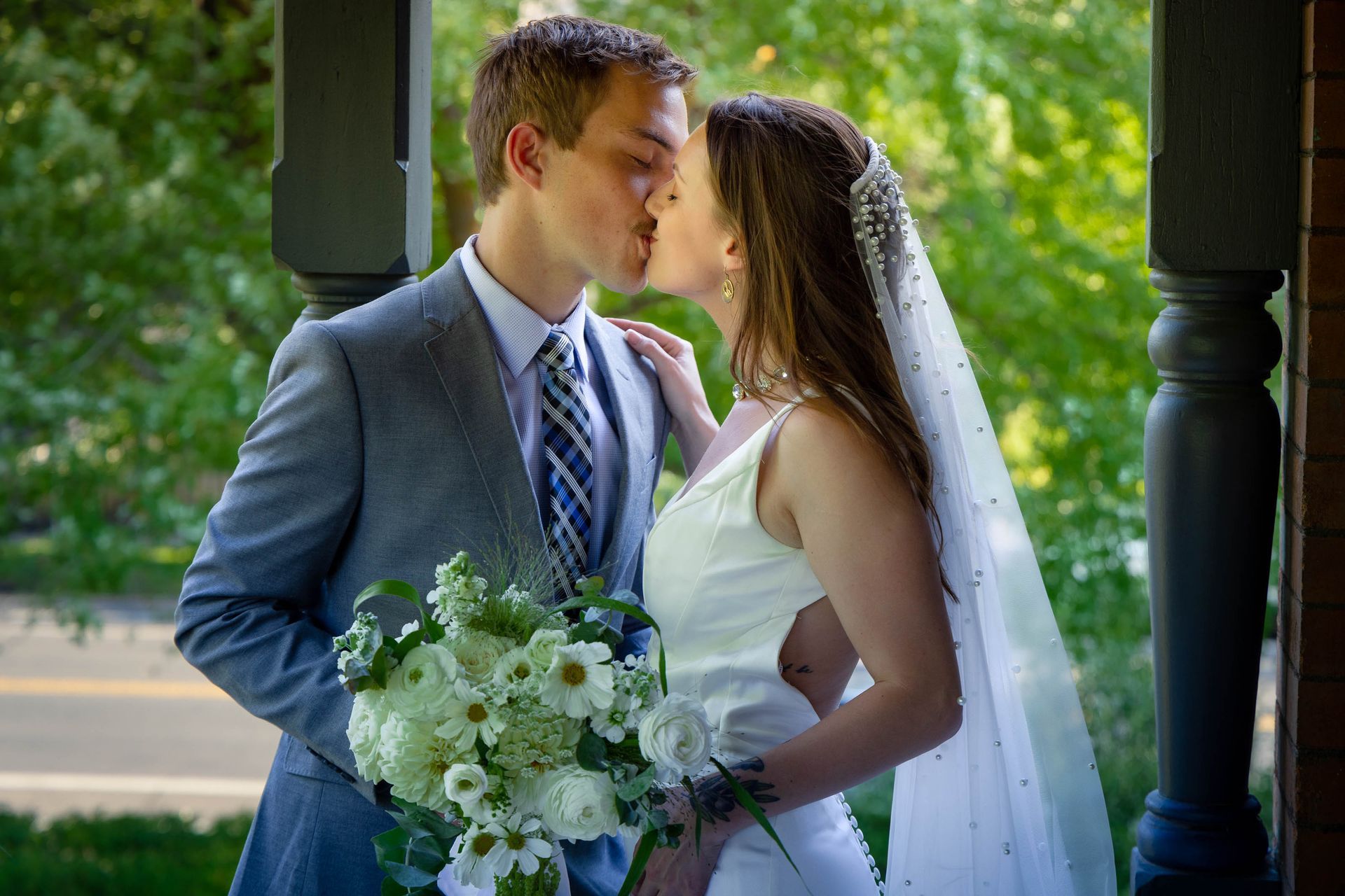 Bride and groom kissing under a gazebo, holding a bouquet of white flowers.