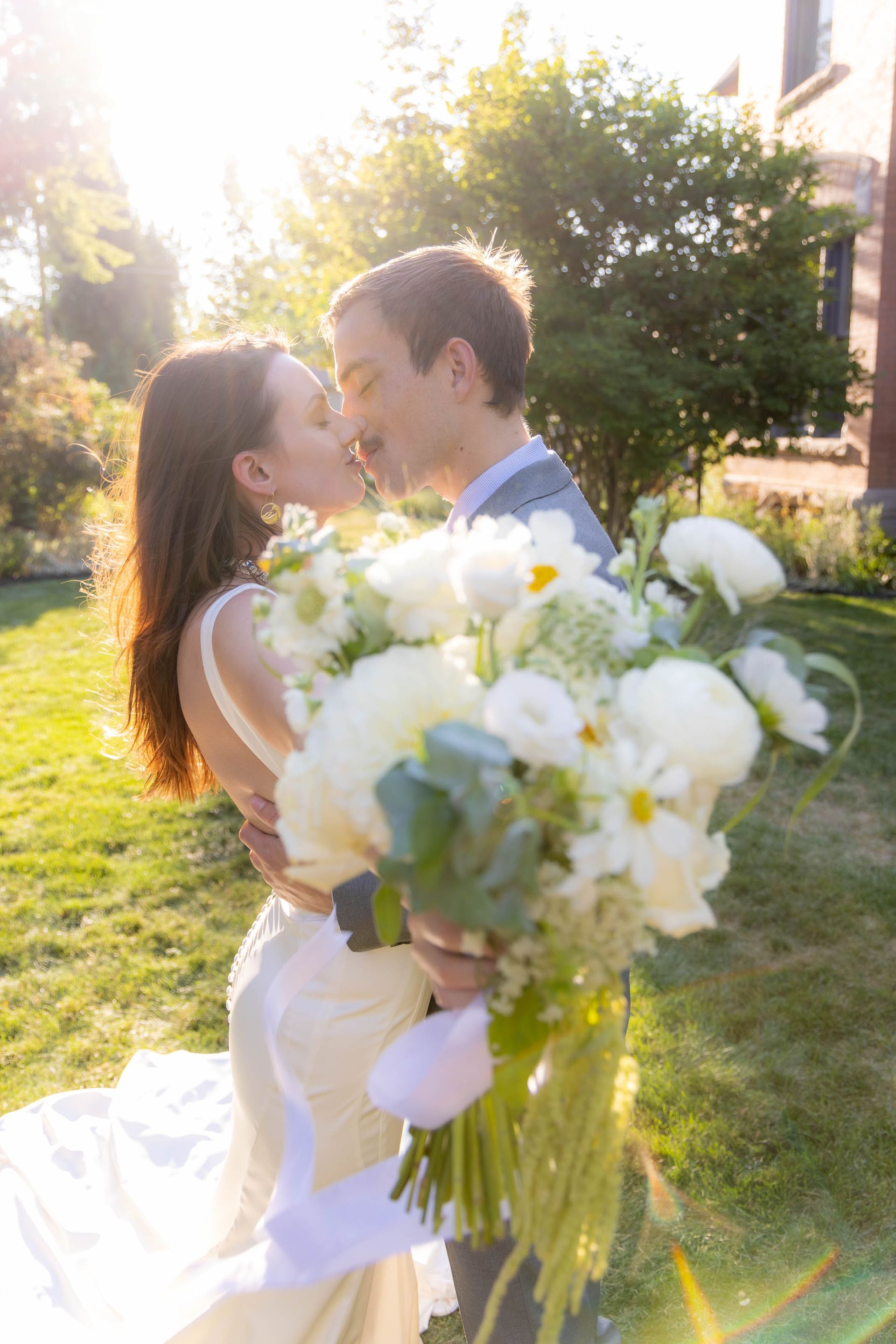 Bride and groom embracing outdoors with a large white bouquet in the foreground