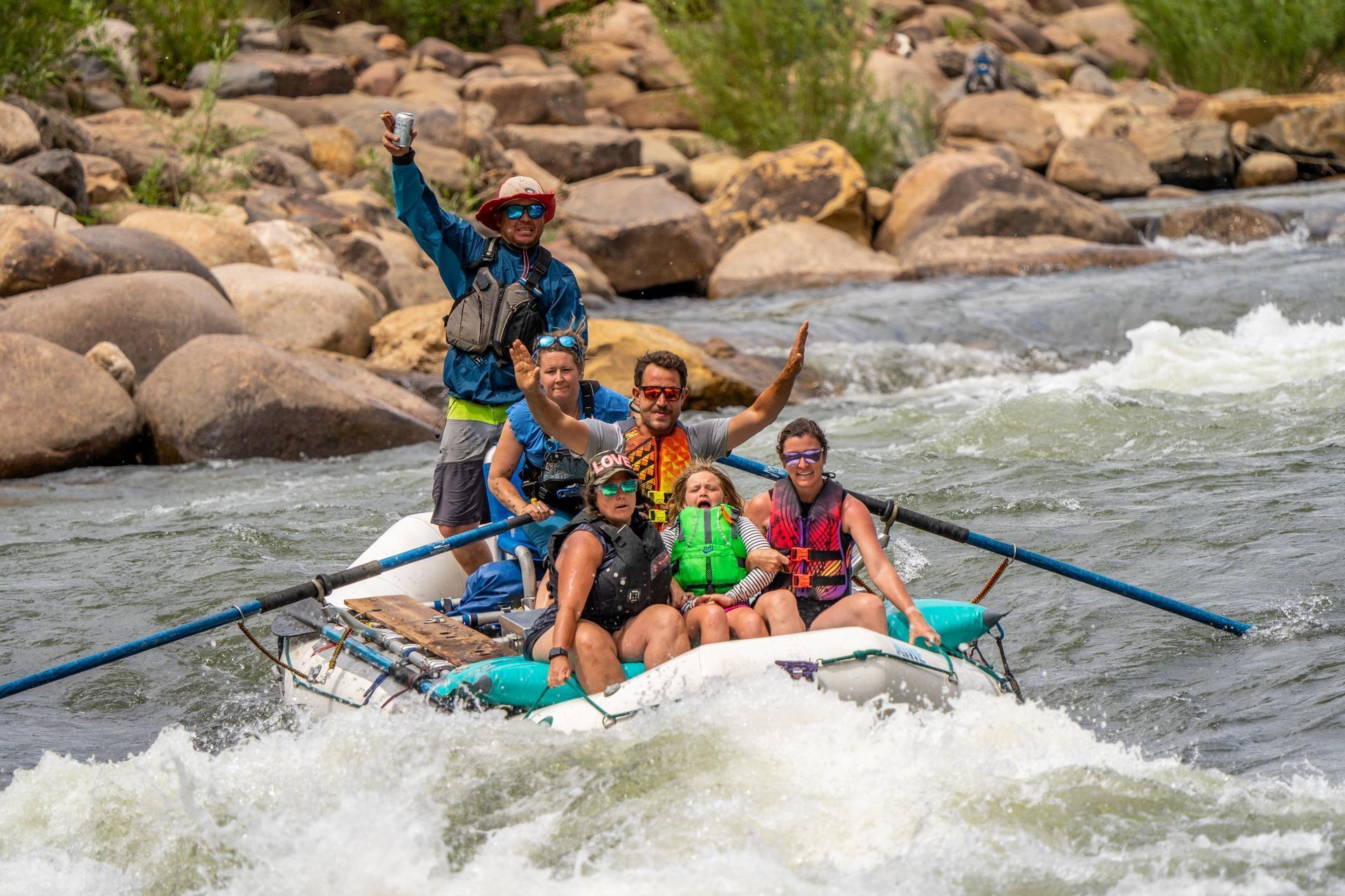 Whitewater rafting team splashing through rapids with rocky riverbank in the background