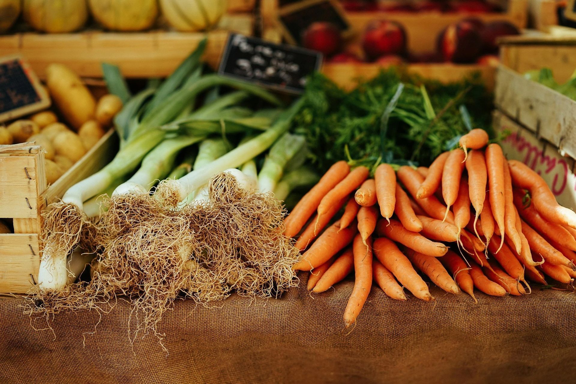 Fresh carrots, leeks, and root vegetables displayed at a rustic market stall with herbs and produce crates