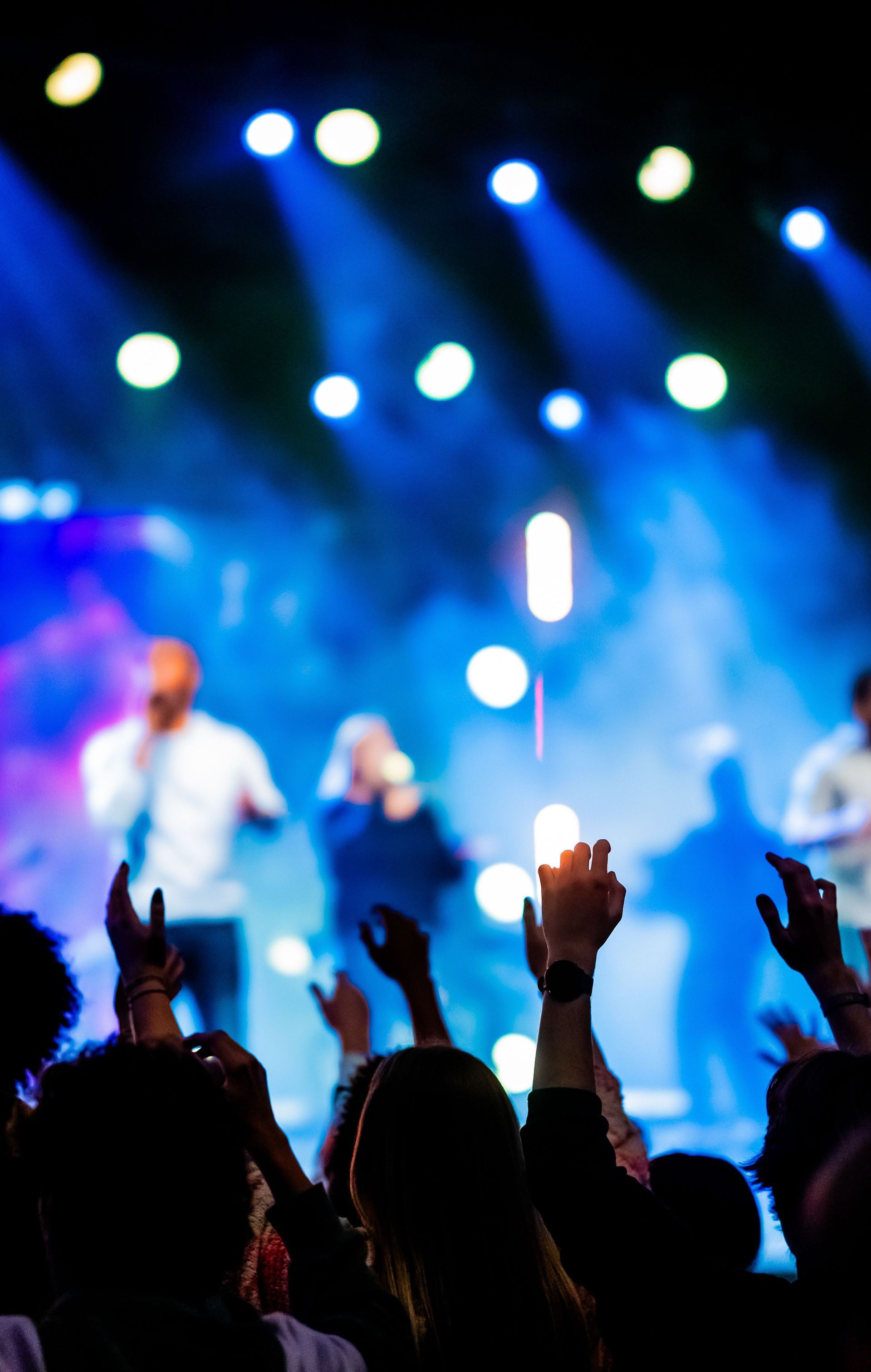 Concert crowd with raised hands facing blue stage lights and blurred performers