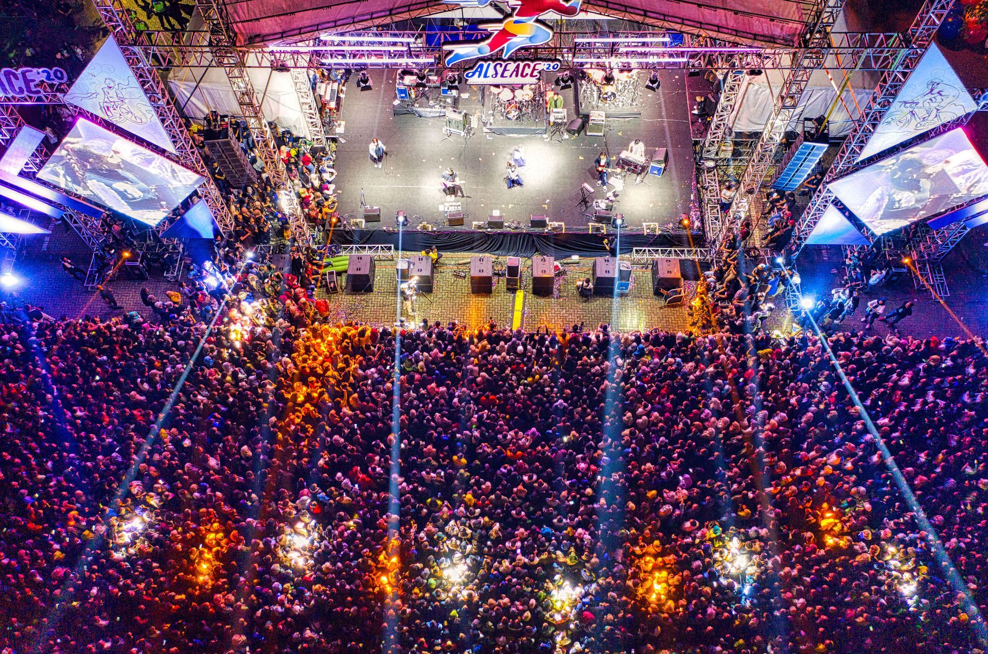 A packed arena with a colorful light show and confetti falling over a concert stage