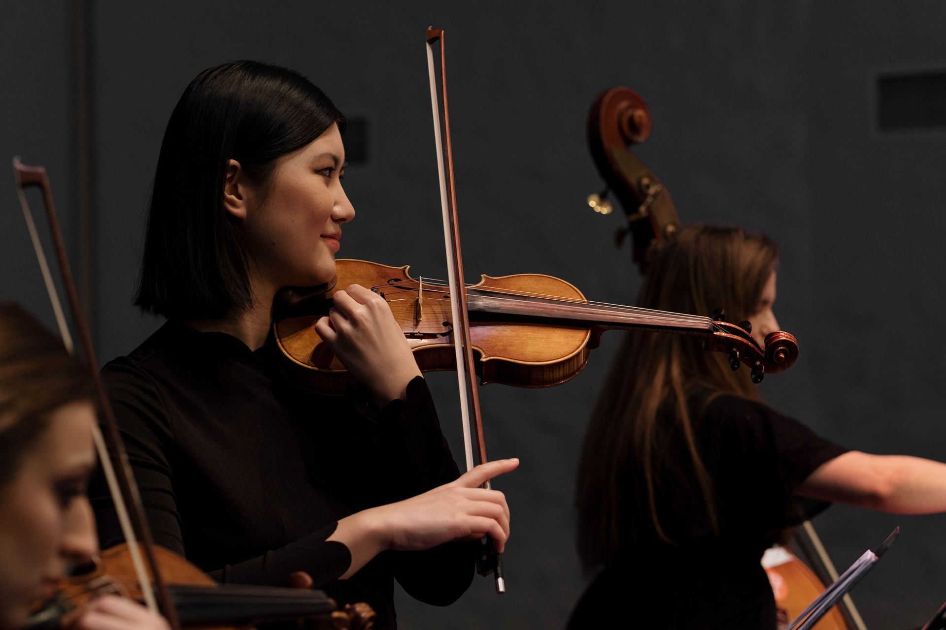 Violinists in a dark concert setting, one musician in focus playing with bow raised