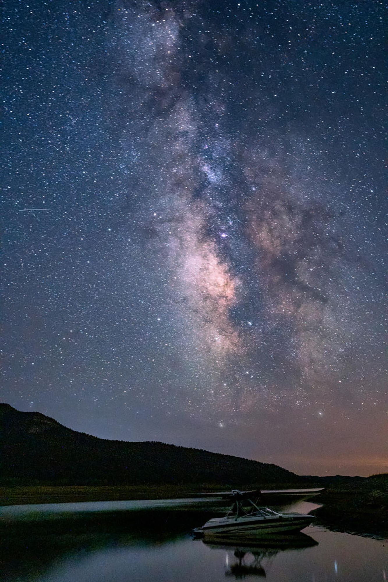 Milky Way above a dark lake with a small dock and boat at dusk