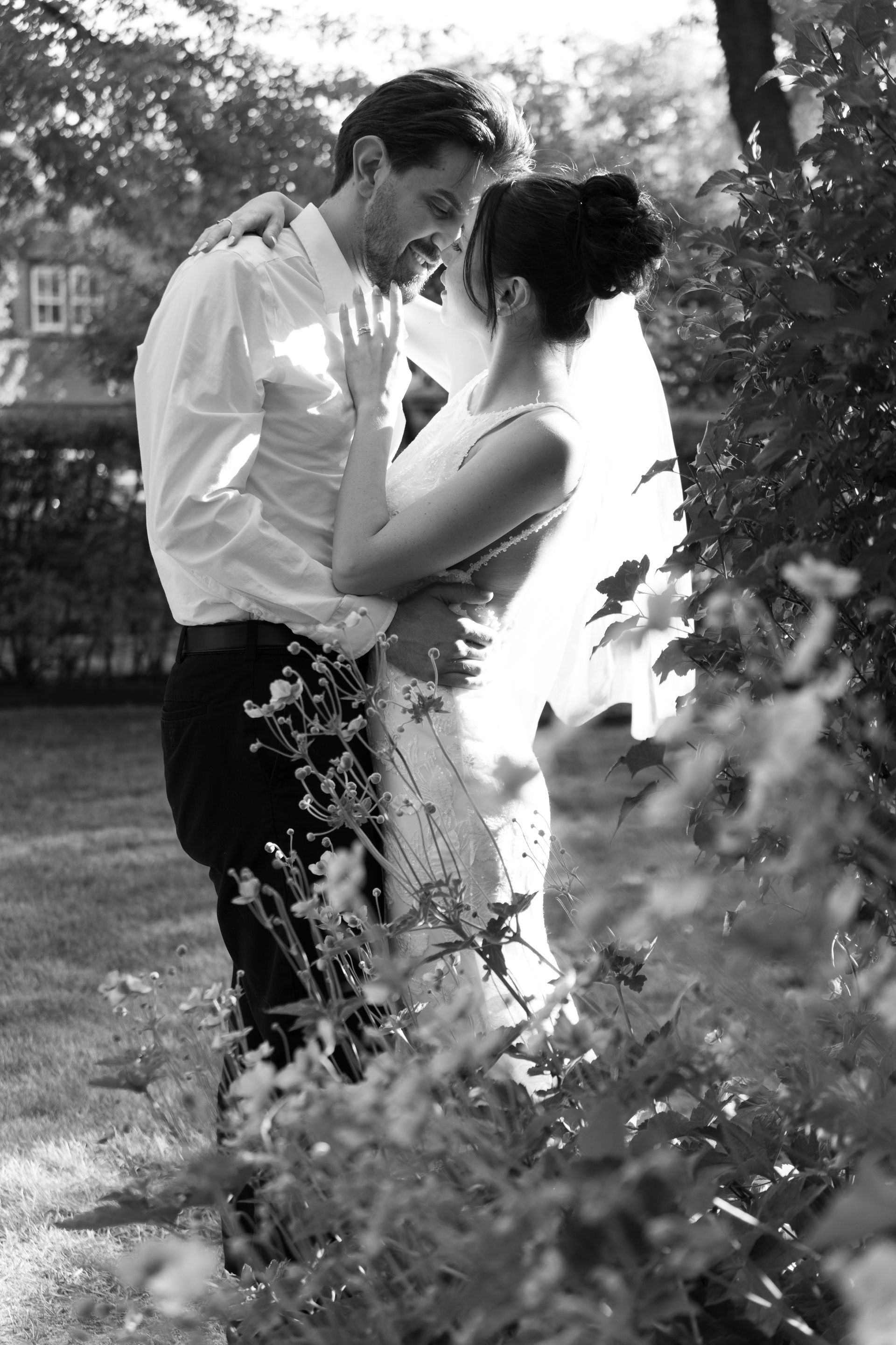 Couple embracing outdoors in a garden, with sunlight filtering through the trees.
