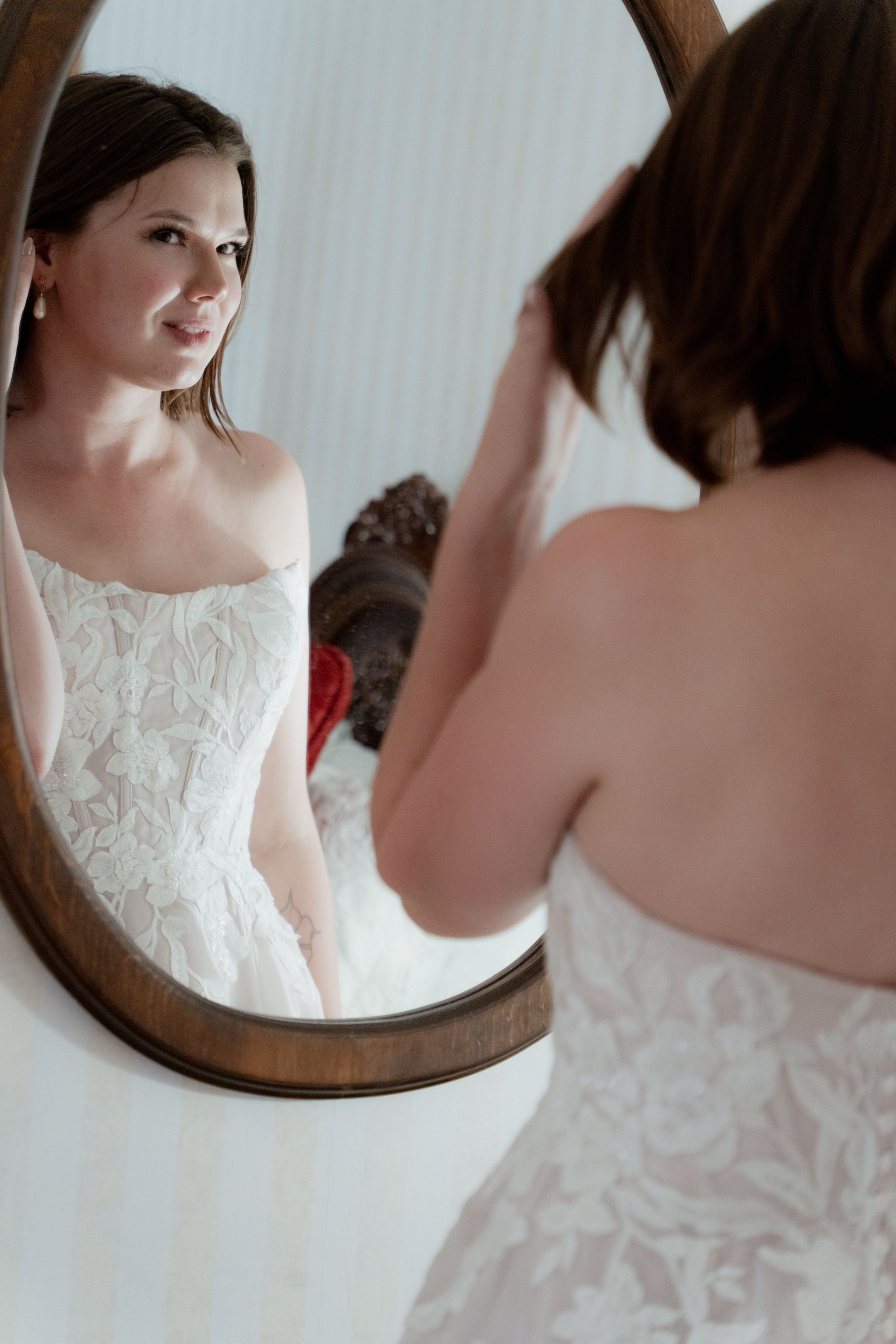 Bride in a white lace dress looking at her reflection in a mirror.