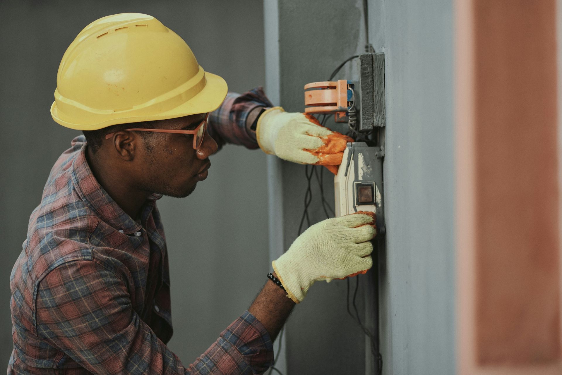 A man wearing a hard hat and gloves is working on an electrical box.