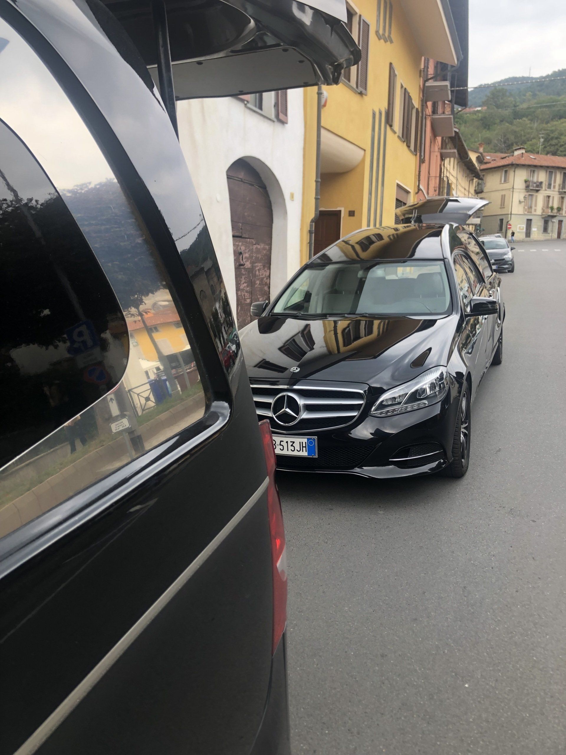 Due carri funebri neri parcheggiati su una strada con un edificio giallo sullo sfondo.