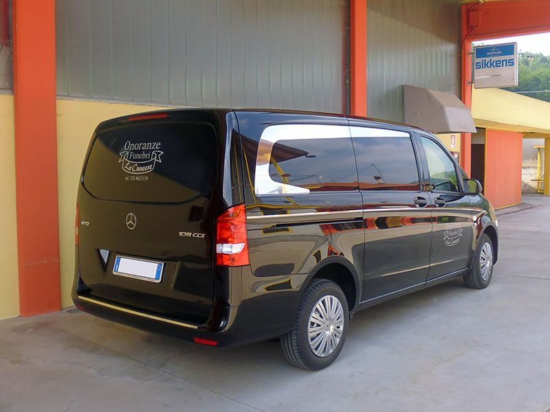 Carro funebre nero parcheggiato davanti a un edificio; finiture argentate; vetri oscurati; scritta 