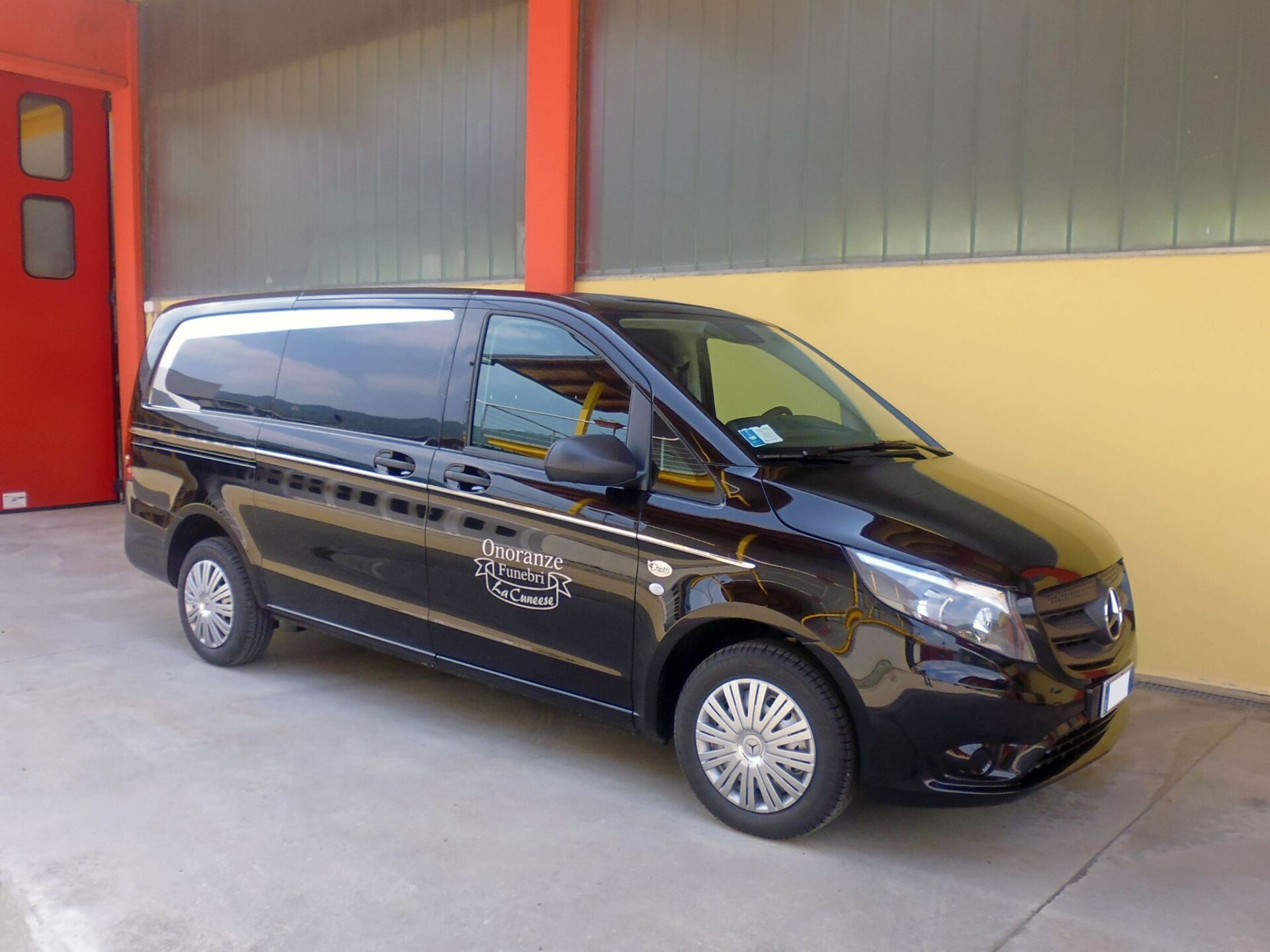 Un furgone Mercedes-Benz Vito nero parcheggiato fuori da un edificio con pareti rosse e gialle.