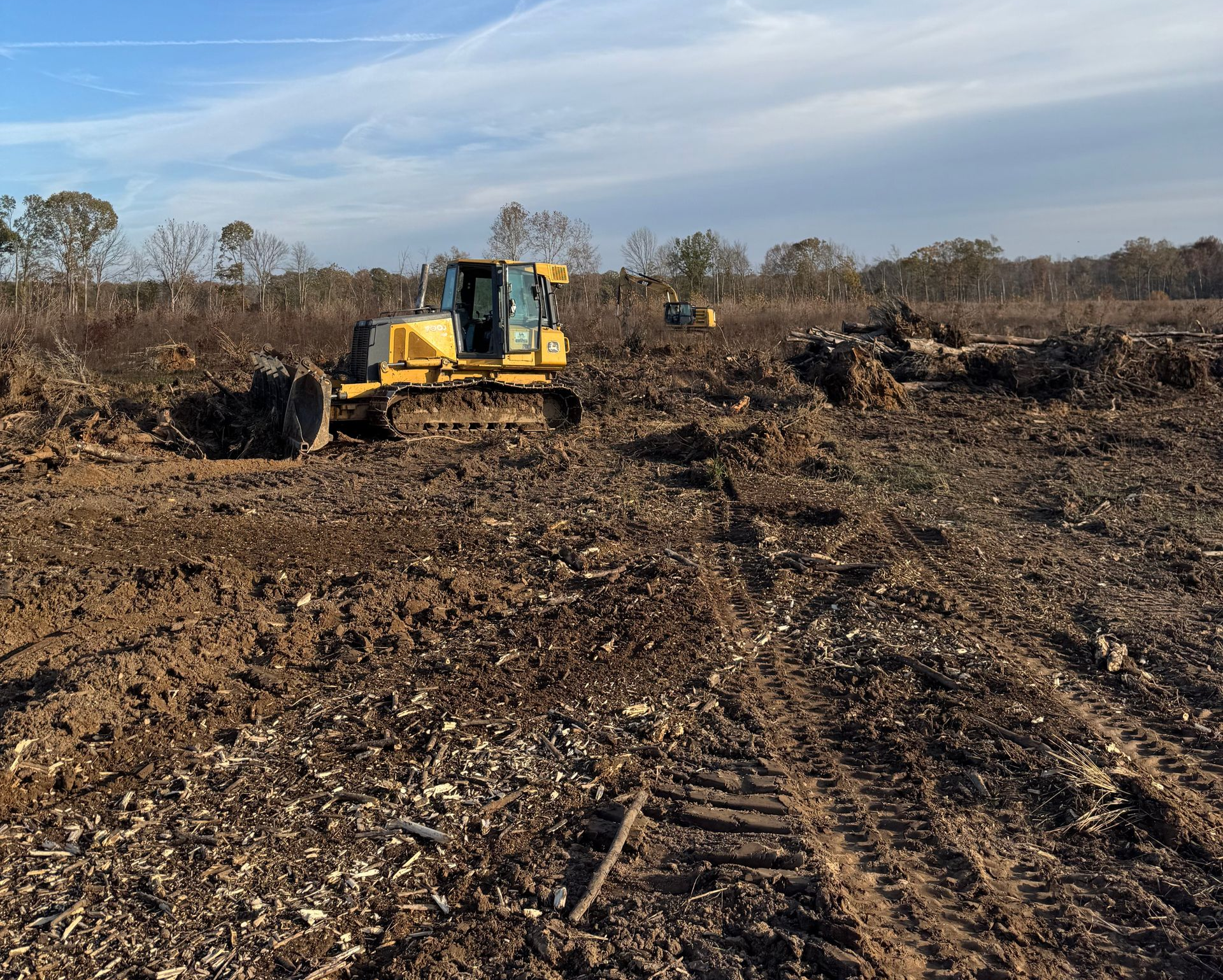 Yellow excavator clearing brush on a muddy field  in Paducah, KY under a cloudy sky.