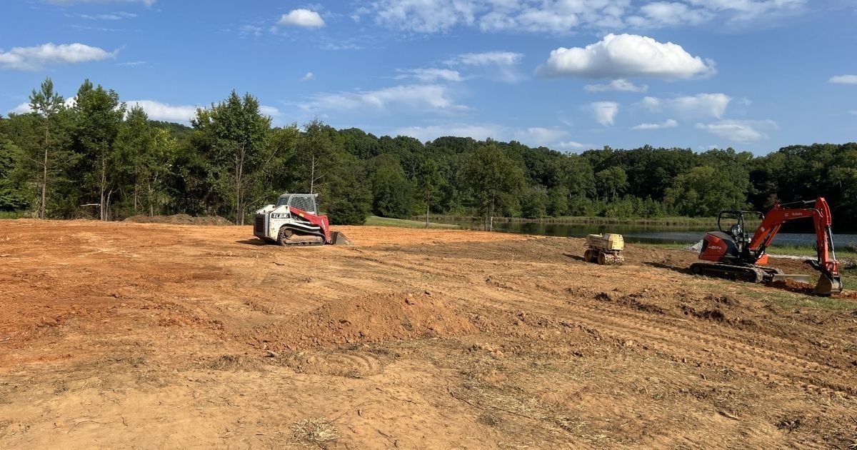Construction site with excavators grading a dirt field under a blue sky