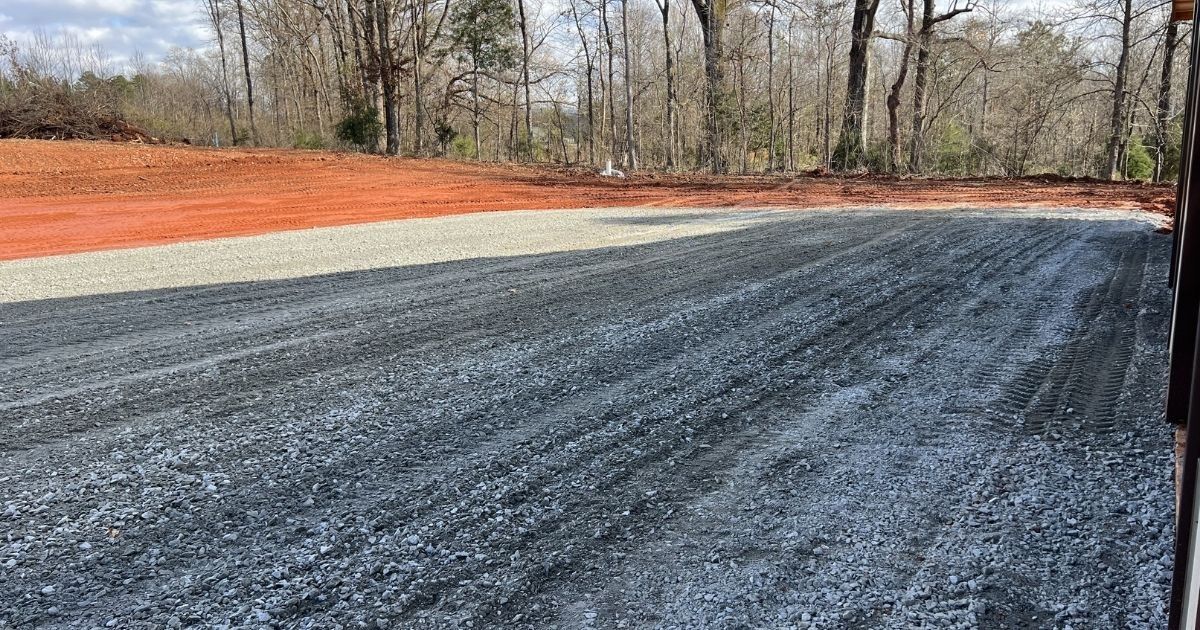 Gravel-covered lot with orange erosion-control fencing and bare trees in the background.