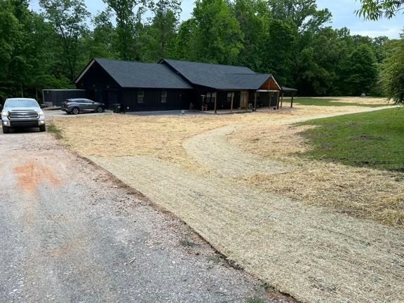 Dark house with gravel driveway and parked cars beside a wooded yard