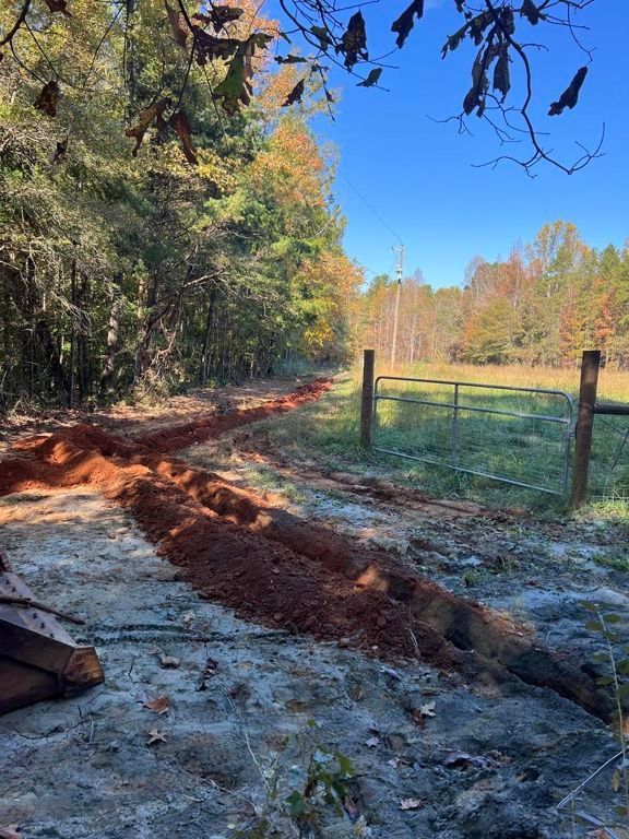 Dirt trench beside a wooded path and fenced field on a sunny day