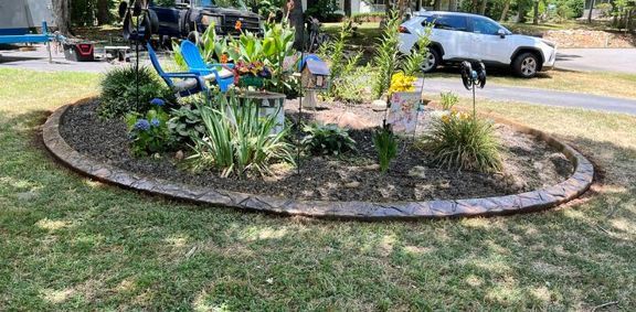 Small landscaped garden bed with flowers and plants beside a sidewalk and parked cars