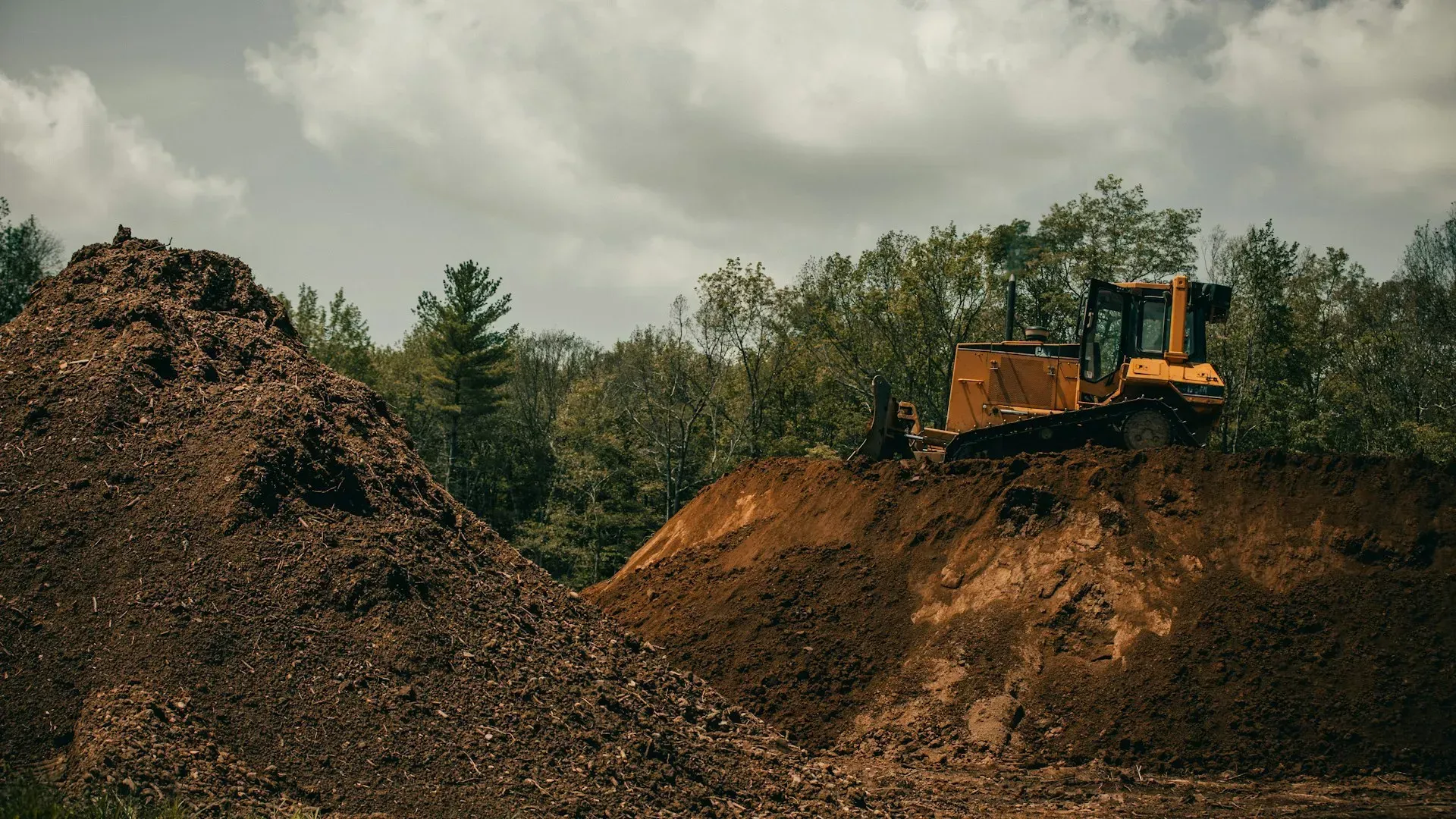 Yellow bulldozer on a dirt mound at a construction site under cloudy skies